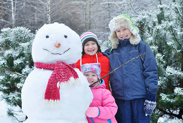 Niños felices en un muñeco de nieve en el invierno. - foto de stock