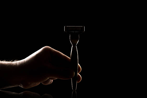 Young man shaving with electric razor. Dark atmosphere with light in the center.