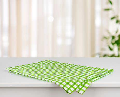 Green checkered kitchen towel on table over defocused curtain background