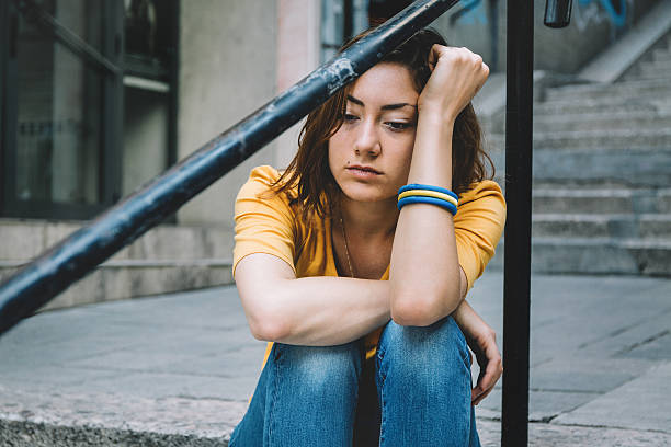 Depressed/Sad girl Teenager sitting on stairs in the city. Wearing black hooded sweatshirt with hood on. gloomy mood stock pictures, royalty-free photos & images