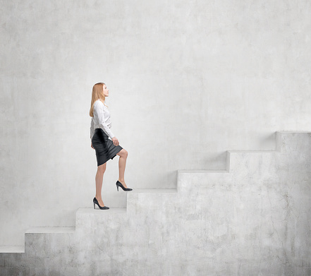 Young businesswoman going up a a concrete stairs steadily along a concrete wall. Concept of career growth.