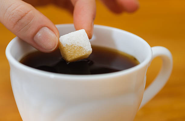 fingers hold a lump sugar piece over cup of tea stock photo