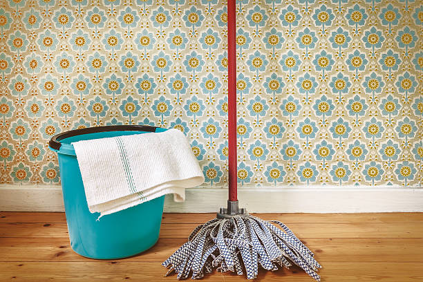Sepia toned image of a floor mop and bucket in front of retro wallpaper