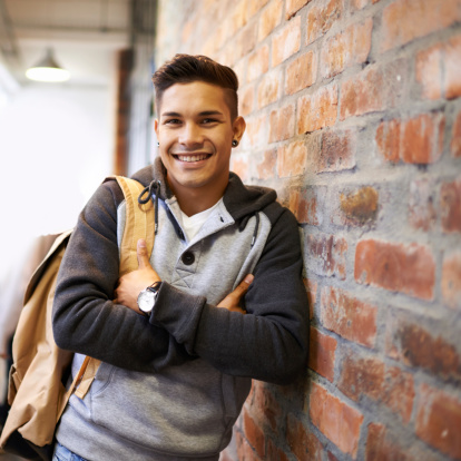 Portrait of a handsome young male student leaning against a wall