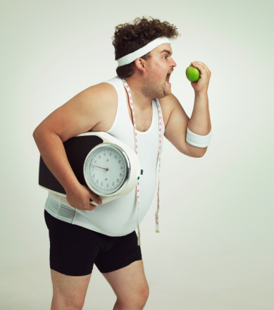 Cropped shot of an overweight man holding a apple,scale and measuring tape