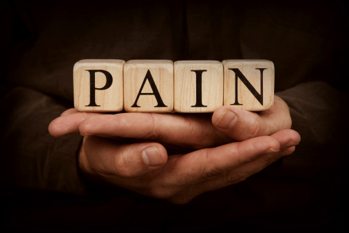Pain spelled out in wooden blocks held in man's hands on a dark background.  Stock image of child's ahlphabet blocks cupped in hands.