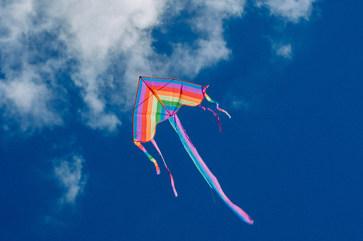Flying kite. Rainbow kite hovers in the air high in the sky. Blue sky with clouds.