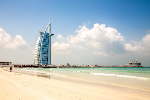 Dubai, United Arab Emirates - March 27, 2014:  External view of the Burj Al Arab in Dubai from the Jumeirah beach.  We see tourist on the beach because it is one of the ideal places to observe this hotel.  The Burj Al Arab is one of the Dubai Landmark, and one of the world's famous and luxurious hotel in the world.