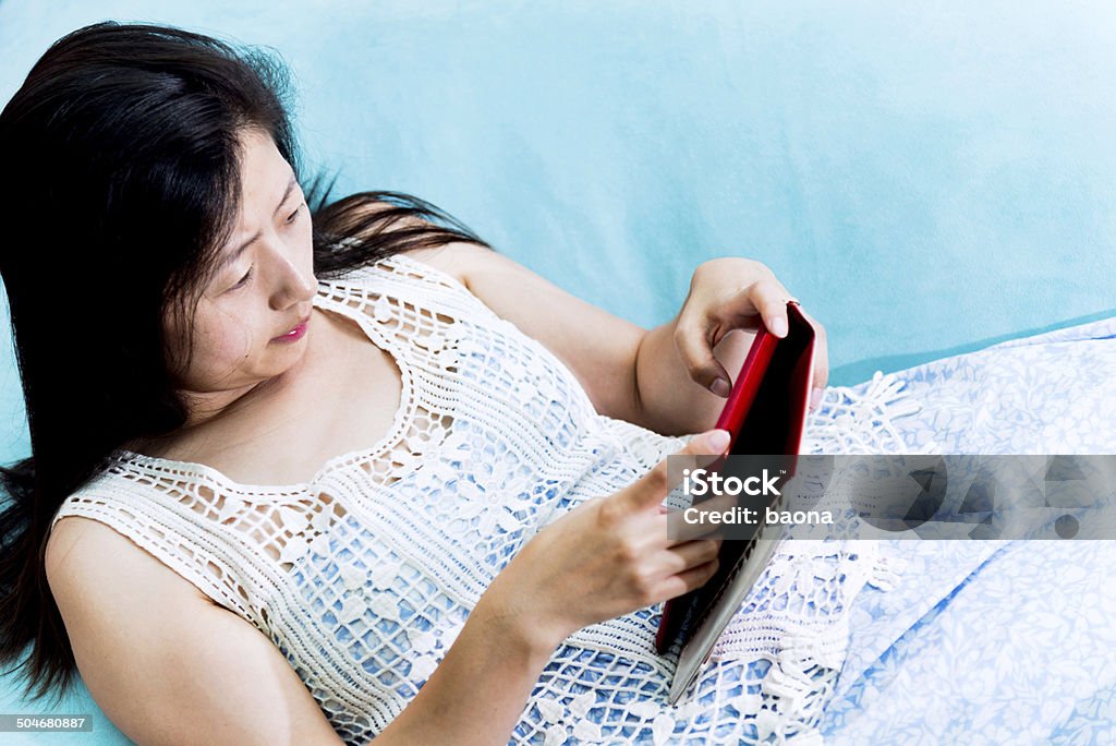 Using tablet computer Asian woman ssing tablet computer at sofa. Adult Stock Photo