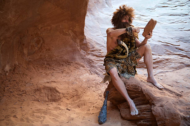 caveman, сидящая на открытом воздухе с использованием камней планшет с сенсорным экраном - neanderthal стоковые фото и изображения
