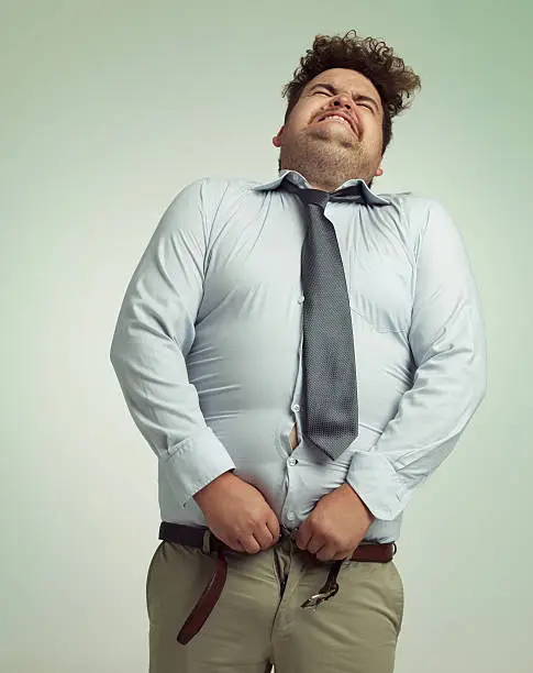 Shot of an overweight man sucking in his stomach to close his pants