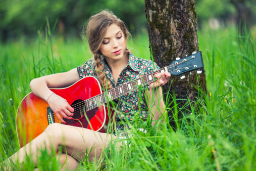 Beautiful young woman playing the guitar in a rural scenery.