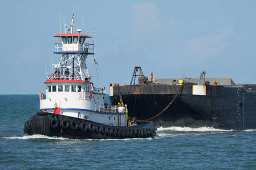 An ocean tugboat pulls a barge inblue ocean water