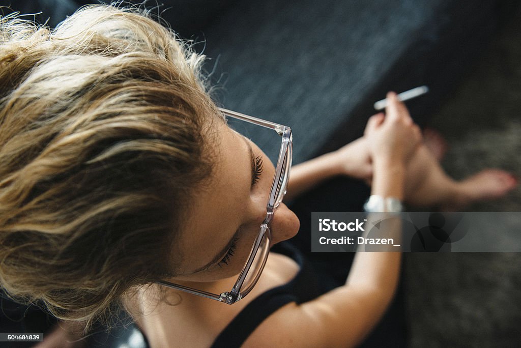 Portrait of brunette with glasses and cigarette from above young woman shot from above, selective focus on eyes, sitting and holding a cigarette Addiction Stock Photo