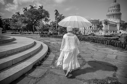 Havana, Cuba - November 6, 2015: Large plaza at the center of old Havana, near Capitolio. Woman in white, with white umbrella walking by the fountain's steps. One of the 