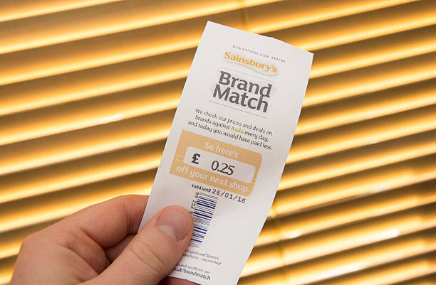 Sainsbury's Brand Match Voucher Poole, UK - January 13, 2016: Holding a Sainsbury's 'Brand Match' voucher given at the check out in a supermarket. It says that Asda would have been £0.25 cheaper and gives 25p off the next shop at Sainsbury's. Other text and information on the voucher.  asda photos stock pictures, royalty-free photos & images