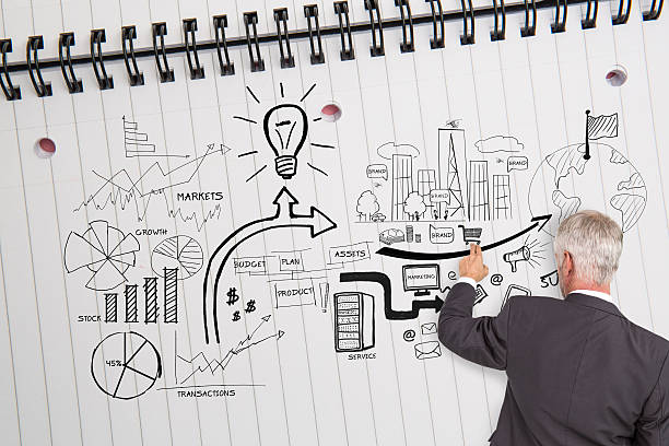 istock Rear view of businessman pointing at illustrations on huge noteb 504704989