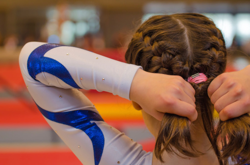 Young gymnast girl fixing her hair with ponytail before appearance on the local competition