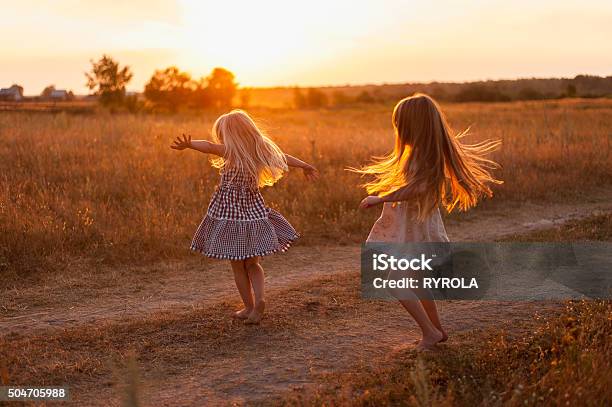 Dos Chicas Bailando En Un Campo Al Atardecer Foto de stock y más banco de imágenes de Hijos - Hijos, Niño, Puesta de sol