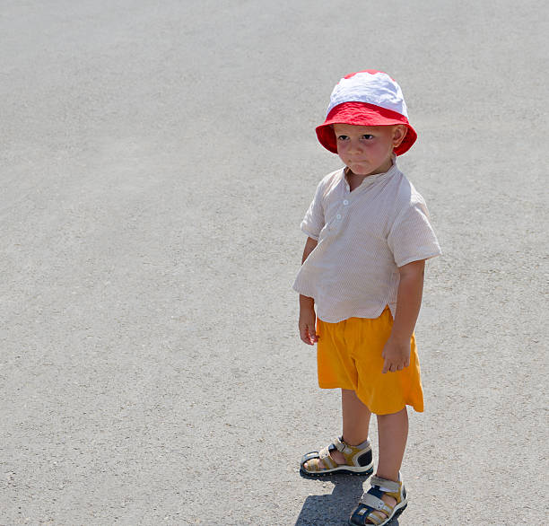 Cute little boy in sunhat and shorts standing on the beach during a summer vacation with copyspace