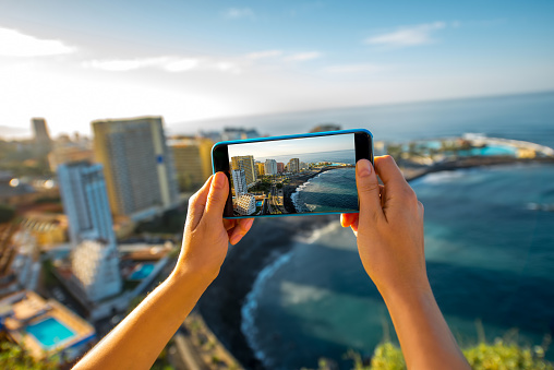 Femaile tourist photographing with smartphone Puerto de la Cruz City on Tenerife island
