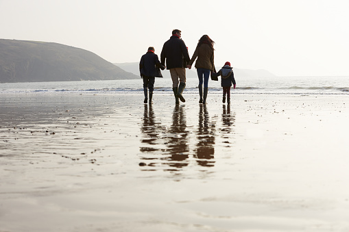 Rear View Of Family Walking Along Winter Beach Holding Hands