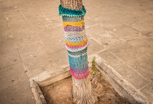 Knitting street art, called yarn bombing or yarnstorm, in a town in Barcelona, Spain. A tree is dressed with knitted colourful wool, giving an artistic nice mood to a dull corner in the city  and making passers-by smile.