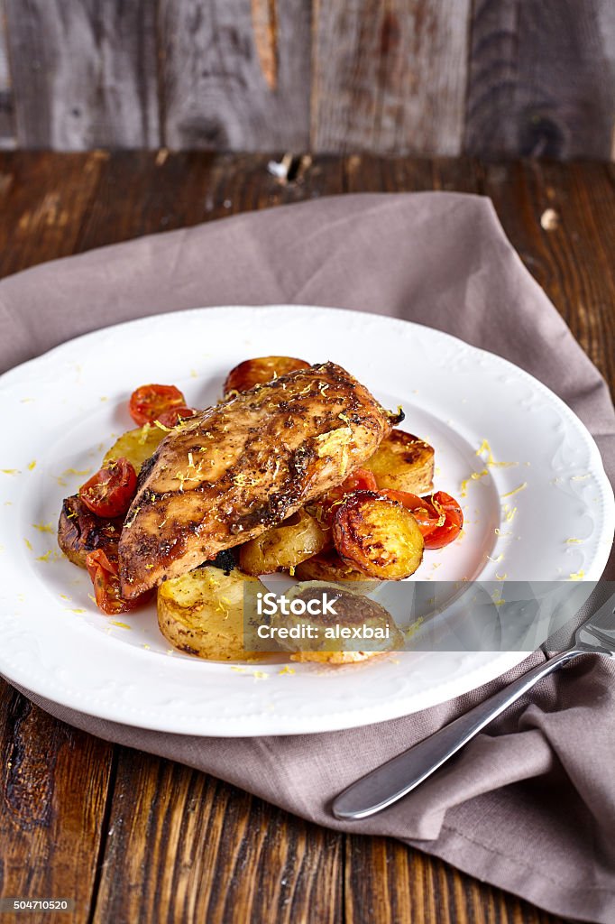 Roasted chicken breast with vegetables Roasted chicken breast in honey-balsamic marinade with potatoes and cherry tomatoes on white plate and wood background Appetizer Stock Photo