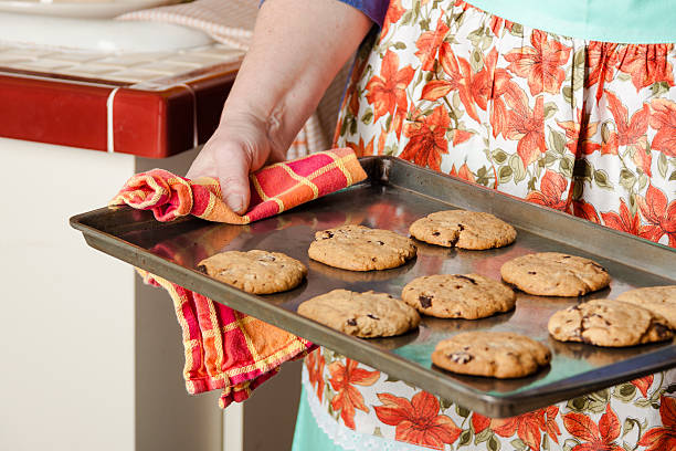 Fresh baked cookies Woman in apron taking hot cookies from oven retro 1950s kitchen stock pictures, royalty-free photos & images
