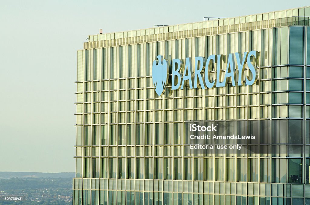 Barclays tower, Canary Wharf London, UK - July 1, 2014:  Evening close up of the top of the very tall office block used by Barclays Bank with their logo overlooking Canary Wharf and Docklands in the East of London. Barclays - Brand Name Stock Photo