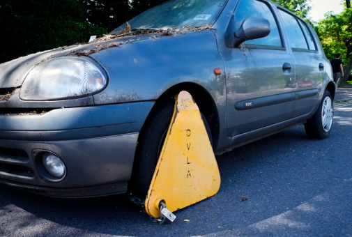 Beckenham, Kent, England - June 6, 2014: A car which has probably been stolen then dumped by the side of a road on South London/Kent borders. It has subsequently collected a DVLA clamp which would prevent it being moved. The DVLA (Driver and Vehicle Licensing Agency) probably attached the clamp via an outside agency because the vehicle appeared not to be taxed. (Background person.)