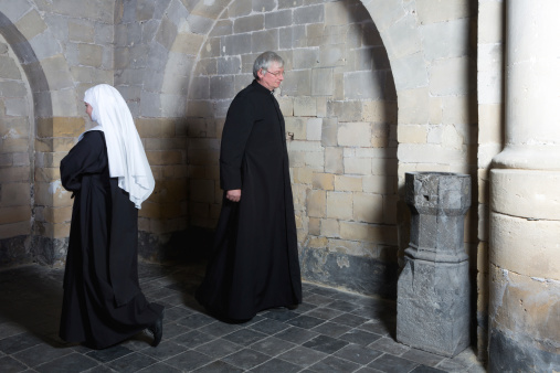 Nun passing a priest along the walls of a medieval church