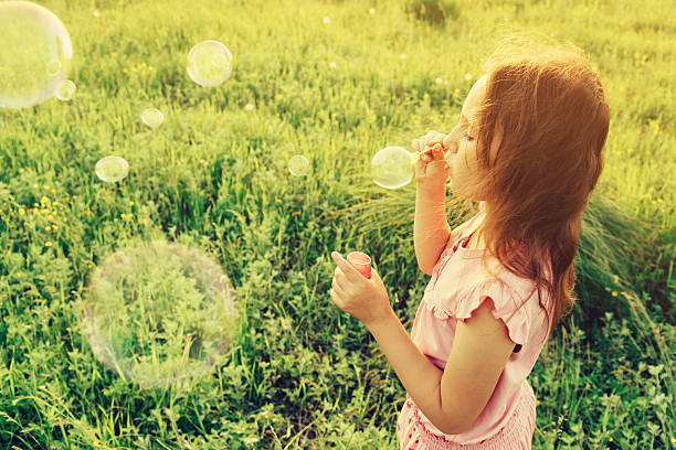 istock Girl is blowing a soap bubbles in summer field 504742307