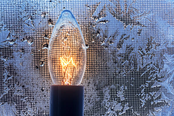 Electric holiday candle warmth melts frost from cold winter window. A little bit of warmth can melt a world of cold.