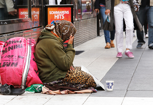 Stockholm, Sweden - June 24, 2014: An unknown woman sits quietly and asking for money with a mug in front of her on Drottninggatan.