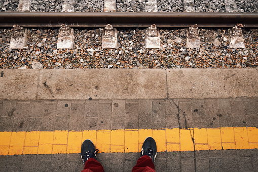 Standing at the yellow lines of an Italian railway station's platform. Many cigarette butts are visible that litter the track. Waiting for the train to arrive