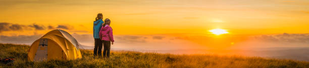 Children camping on mountain ridge looking into golden sunset panorama