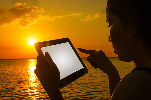 istock Silhouette woman with digital tablet in hands at sunset beach 504749476