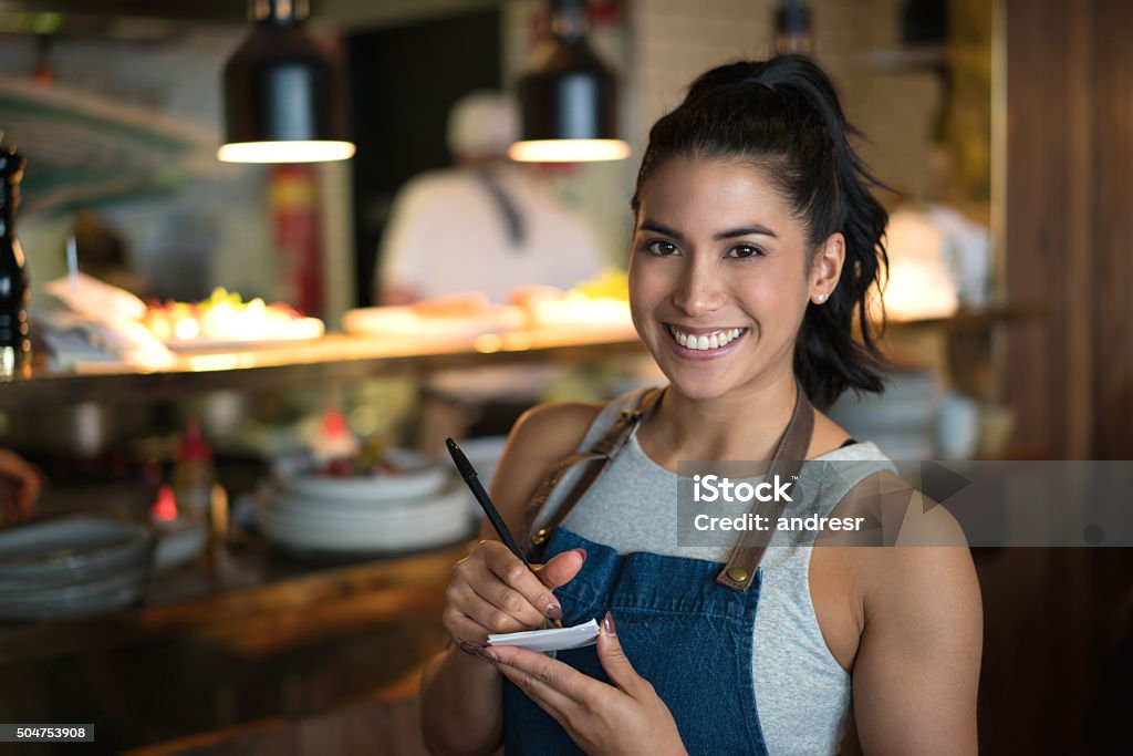 Happy waitress working at a coffee shop Happy waitress working at a coffee shop and looking at the camera holding a notepad Waitress Stock Photo