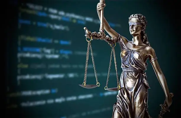 Photo of Justice statue with code on screen in background