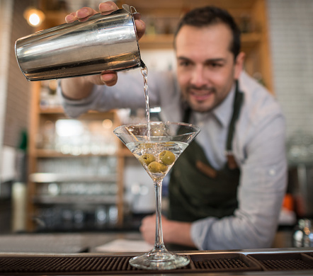 Barman making a martini cocktail at a bar and pouring it into a glass