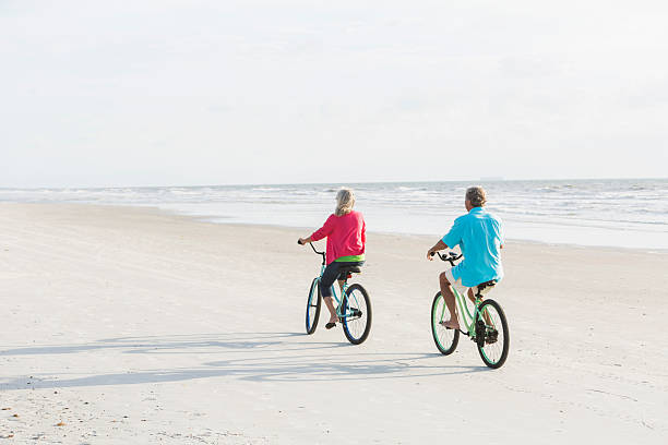 vue arrière d'un couple d'âge mûr équitation vélos sur la plage - senior couple cycling beach bicycle photos et images de collection