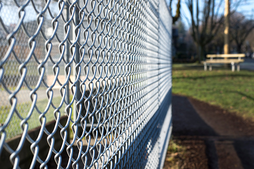 metal fence cage in a soccer field, park bench behind, sunny day, closeup, detail, horizontal