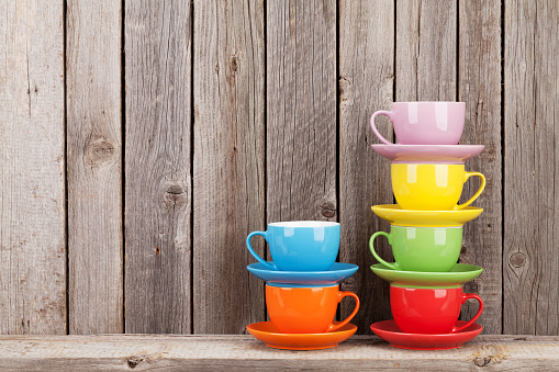 Colorful coffee cups on shelf against rustic wooden wall with copy space