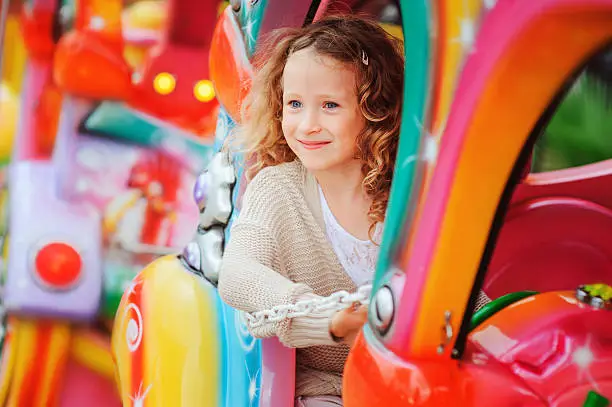 Photo of happy child girl riding train on funfair