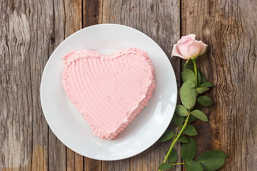 Chocolate cake decorate with pink cream butter. On wood table with pink rose. Top view.