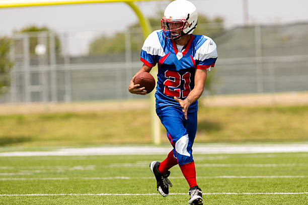 Football player running with ball on playing field. Goal post. One, young adult football player returning the football after a kick off play.  Football field and goal post.  wide receiver athlete stock pictures, royalty-free photos & images