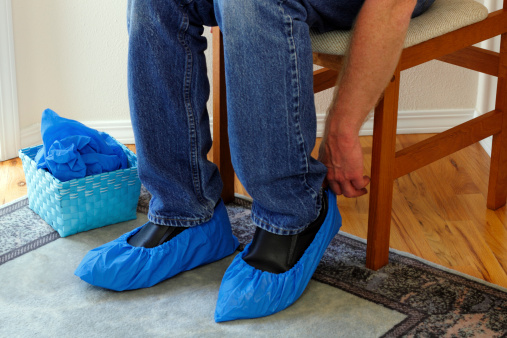 Male who just arrived in a foyer of a home for sale that he is going to tour sits in a chair putting booties on his shoes in order to protect the floors.