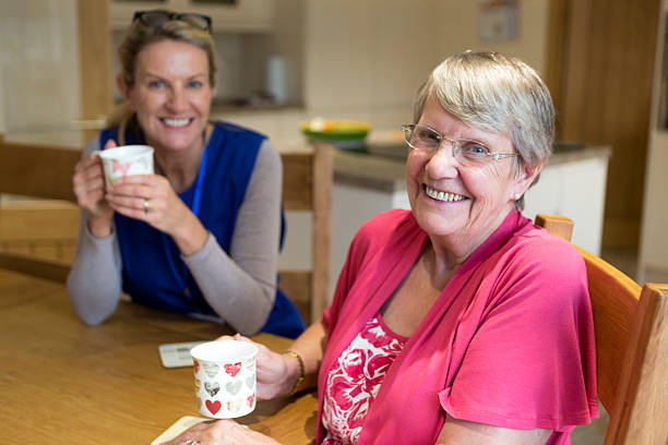 Enjoying the Company! Community care worker joins an an elderly woman for a cup of tea while sitting at her kitchen table. meals on wheels photos stock pictures, royalty-free photos & images