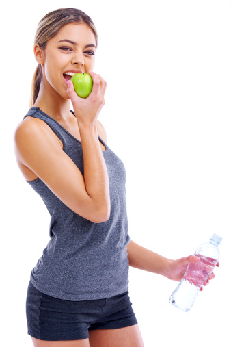 Portrait of a sporty young woman eating an apple while holding a bottle of water